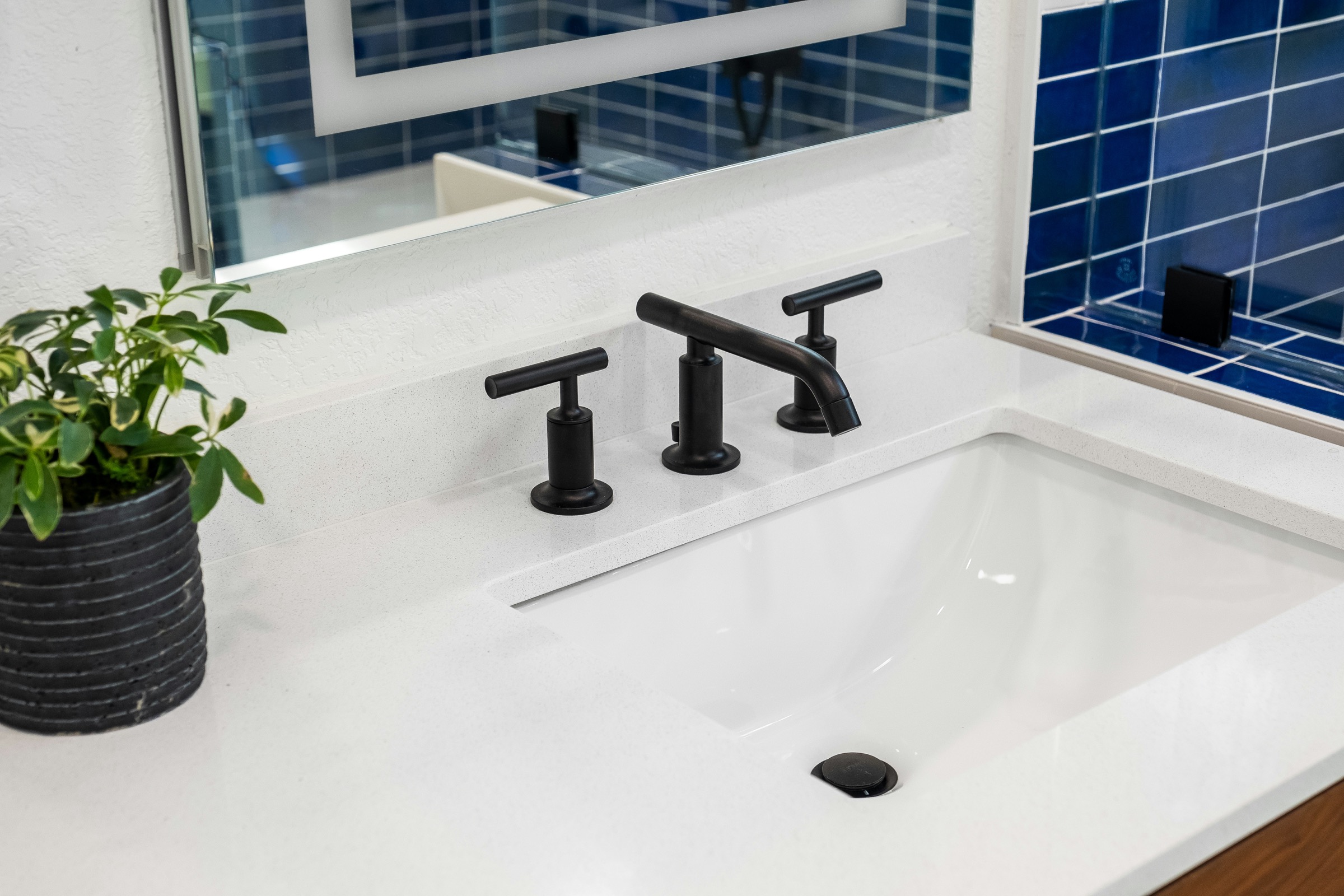 White basin with matte black faucet and blue tiled wall